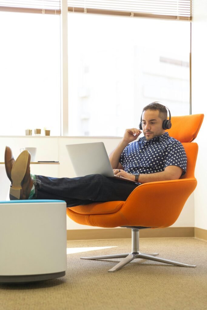 A man relaxes while working remotely in a modern office with a laptop and headphones.